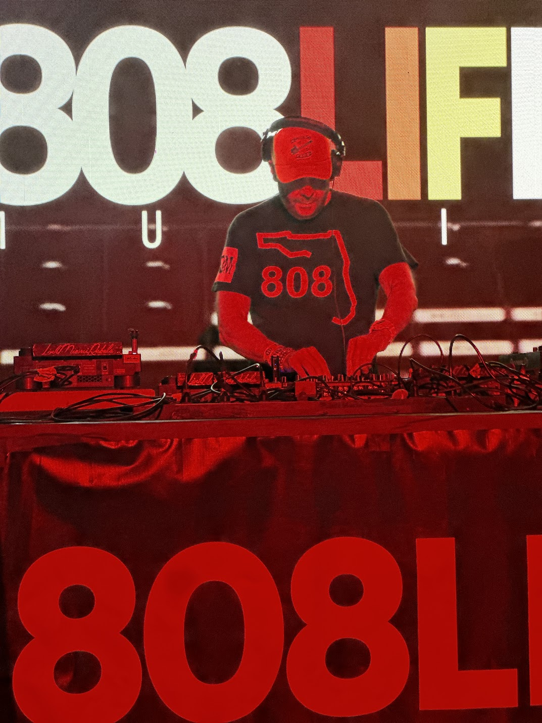 DJ in an 808 shirt performing under red stage lighting
