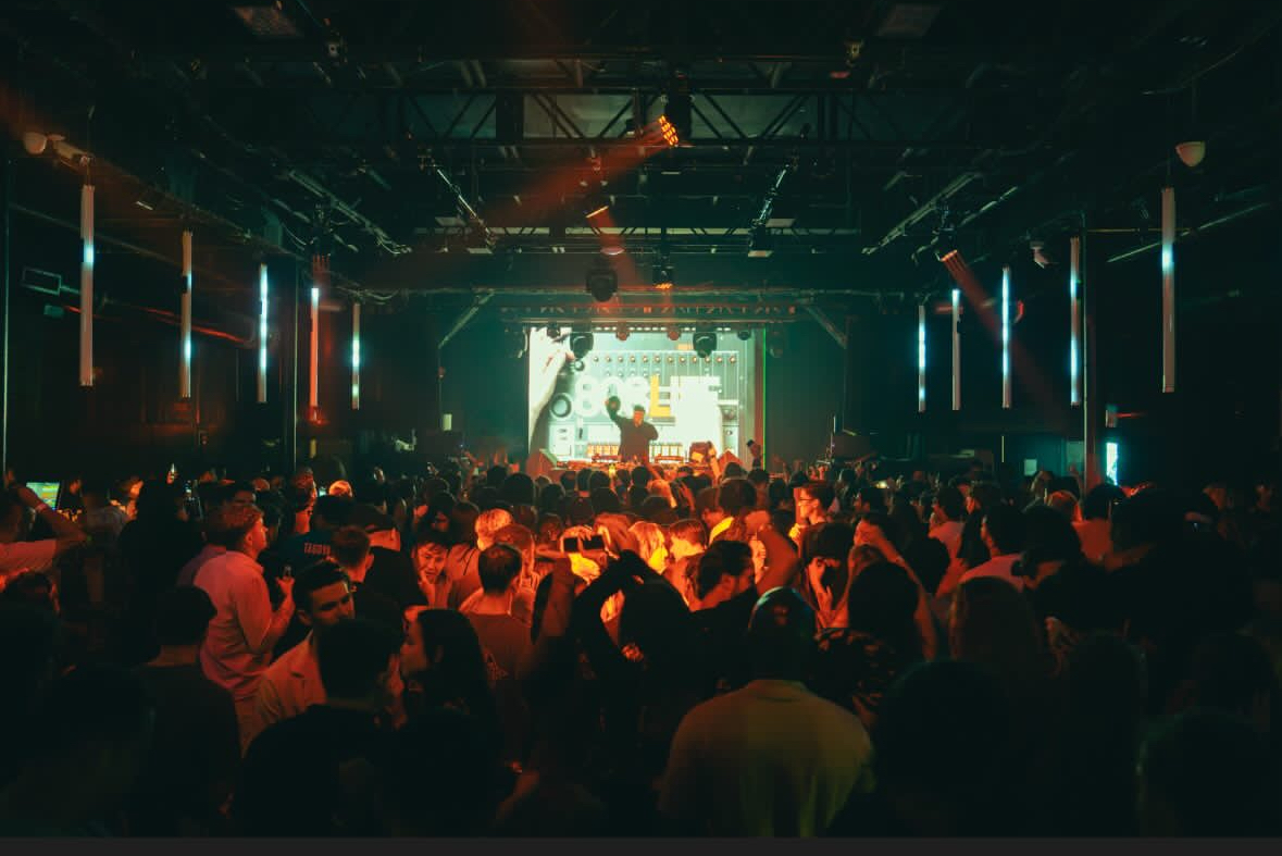 Wide crowd shot of the dancefloor with the 808 Life screen in the distance