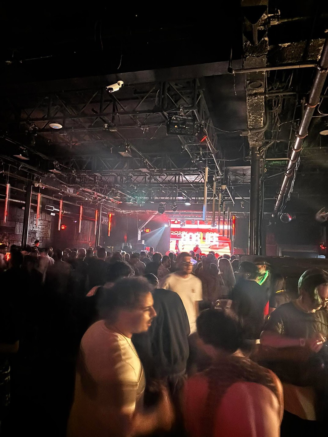 Packed crowd facing the lit 808 Life stage from the back of the room
